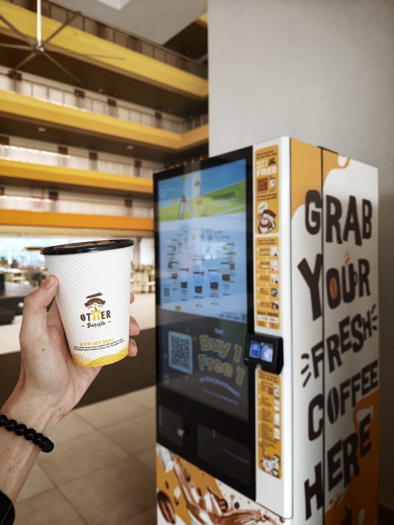 Otter robotic barista machine dispensing fresh espresso drinks to office workers during their morning rush in a Klang Valley corporate lobby.