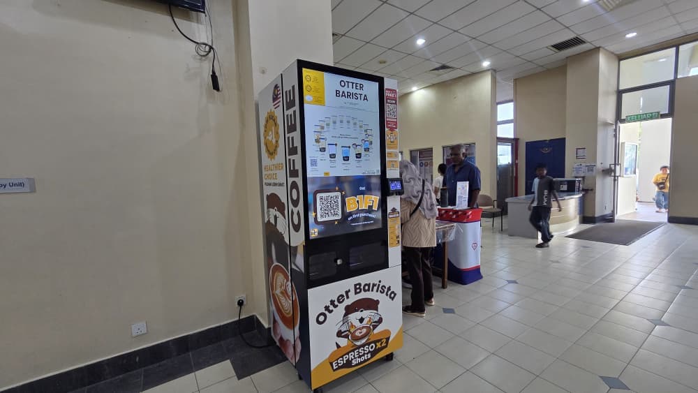 Otter robotic barista dispensing specialty coffee to suited professionals during morning break in a modern Klang Valley office lobby.