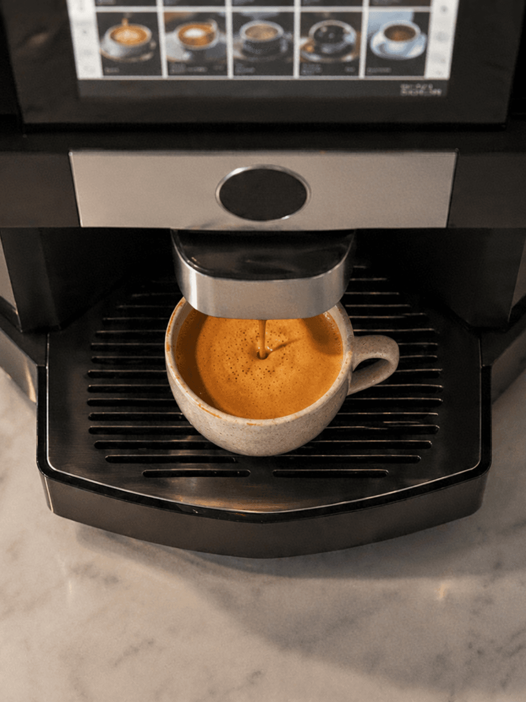 Close-up of an Otter robotic barista dispensing a fresh espresso shot into a ceramic cup at an office pantry station in Kuala Lumpur.