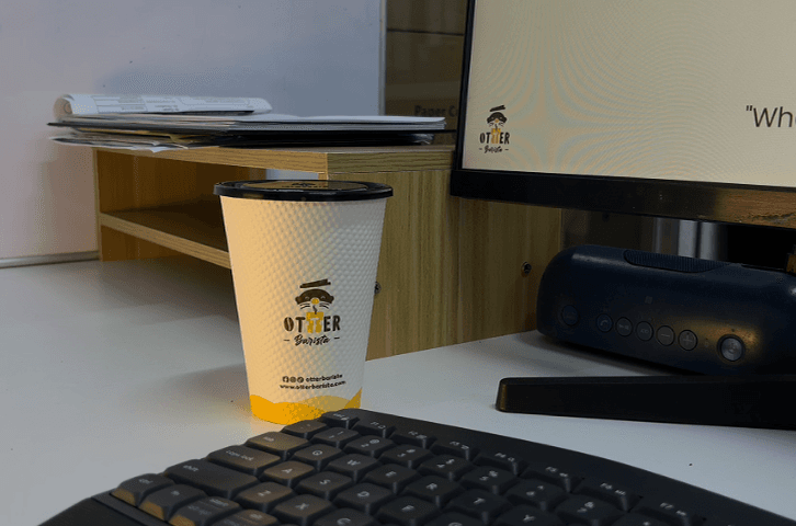 A sleek Otter robotic barista dispensing espresso drinks at a modern Malaysian office reception desk during morning rush hour.